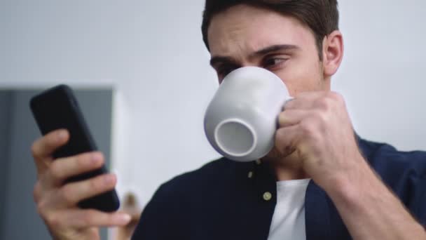 Retrato del joven escribiendo teléfono móvil en la cocina del hogar. Chico bebiendo café — Vídeos de Stock