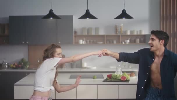 Pareja joven bailando juntos en la cocina casera. Felices amigos divirtiéndose en interiores . — Vídeos de Stock