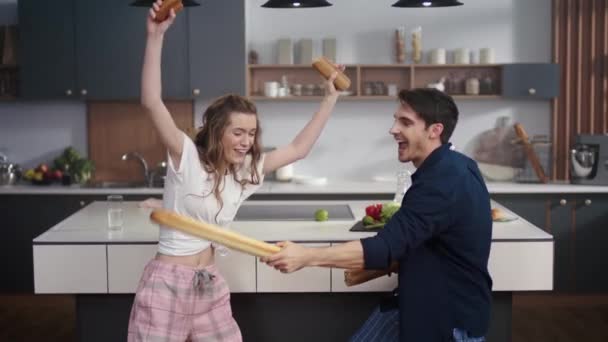 Paar kämpft in der heimischen Küche mit Baguette. Fröhliche Freunde haben Spaß zu Hause — Stockvideo