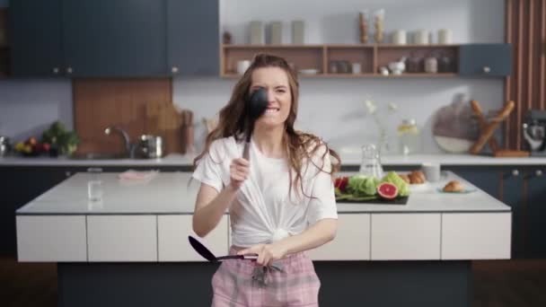 Забавная женщина развлекается на домашней кухне. Милая девушка барабанит с посудой в помещении — стоковое видео