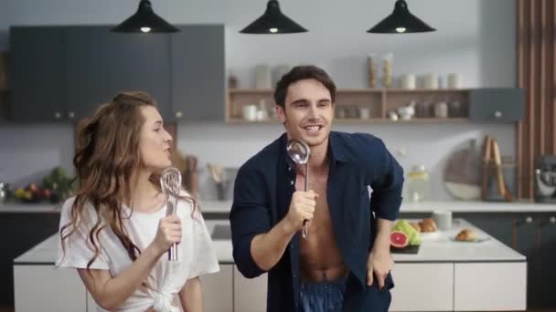 Lustiges Paar singt mit Löffel und Schnurrbart in Zeitlupe in der modernen Küche. — Stockvideo