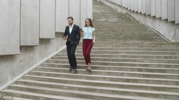 Уверенные коллеги спускаются по лестнице. Мужчина и женщина разговаривают на улице — стоковое видео