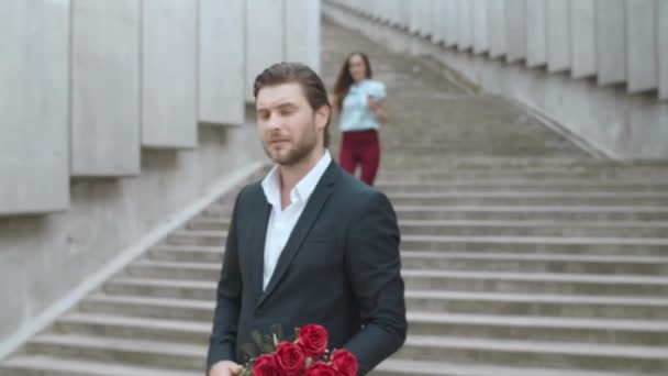 Ο φίλος με τα λουλούδια περιμένει την κοπέλα του. Αντρας και γυναίκα συναντιούνται — Αρχείο Βίντεο