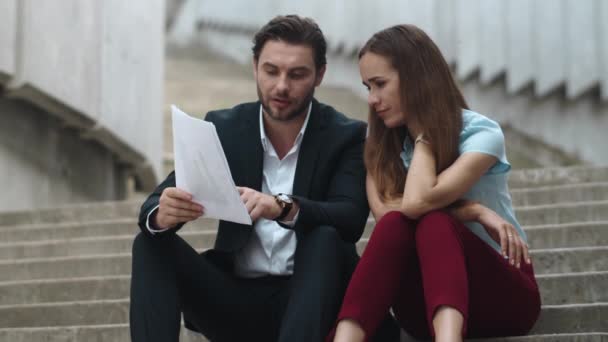 Уставший бизнесмен и деловая женщина просматривают деловые документы на улице — стоковое видео