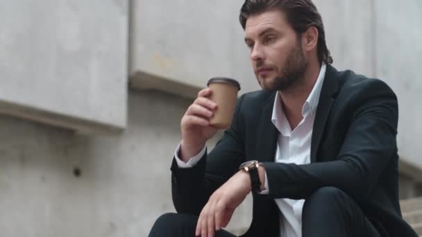 Az üzletember, aki iszik, kávét visz magával a városba. Férfi munkás ül a lépcsőn — Stock videók