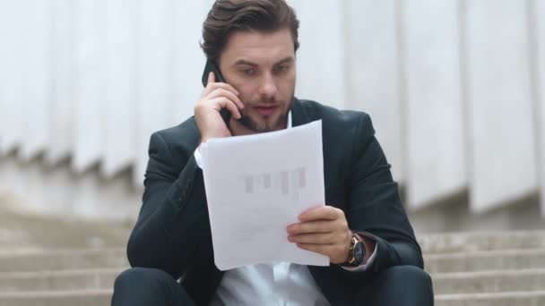 Businessman having conversation on cellphone at street. Man sitting on stairs — Stock Video