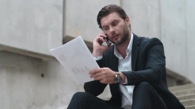 İş adamı müşterisiyle akıllı telefonda konuşuyor. Dışarıdaki belgelerle çalışan adam.