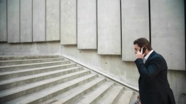 Belgeleri olan bir iş adamı merdivenlerden çıkıyor. Erkek işçi akıllı telefondan konuşuyor.