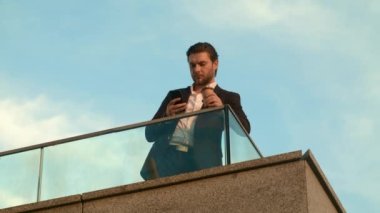 Şehirde akıllı telefon kullanan bir iş adamı. Müdür elinde kahveyle balkonda dikiliyor.