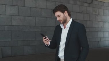 İş adamı caddede akıllı telefondan yazı yazıyor. Heyecanlı adam başarıyı kutluyor.