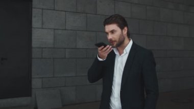 Gülümseyen iş adamı modern şehirde cep telefonundan sesli mesaj kaydediyor.