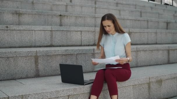 Verrast zakenvrouw controleren van informatie uit documenten op laptop computer — Stockvideo