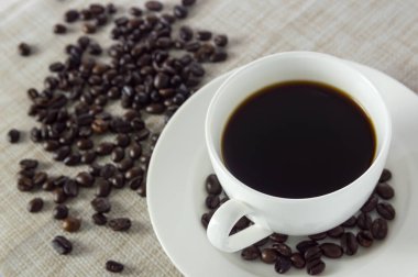 Beyaz bir bardak ve kahve çekirdekleri örtüleri üzerinde siyah kahve