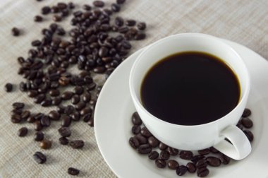 Beyaz bir bardak ve kahve çekirdekleri örtüleri üzerinde siyah kahve