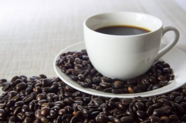 Beyaz bir bardak ve kahve çekirdekleri örtüleri üzerinde siyah kahve