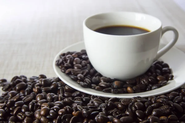 Beyaz bir bardak ve kahve çekirdekleri örtüleri üzerinde siyah kahve