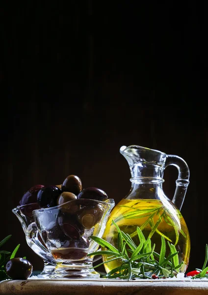 Olives grecques noires et vertes dans des bols en verre avec romarin et huile dans une cruche — Photo