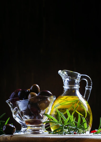 Black and green Greek olives in glass bowls with rosemary and oil in a jug