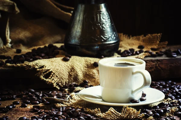 Xícara branca de café preto com espuma, cafeteira turca na velha mesa de madeira — Fotografia de Stock