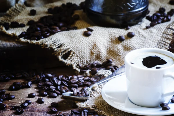 White cup of black coffee with foam, Turkish coffee maker on the old wooden table