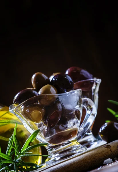 Schwarze und grüne griechische Oliven in Glasschalen mit Rosmarin und Öl in einem Krug — Stockfoto