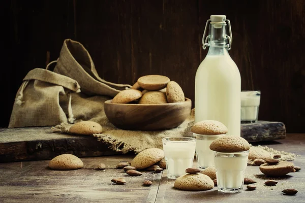 Cow's milk in the bottle and a glass and cookies with almond amaretti — Stock Photo, Image