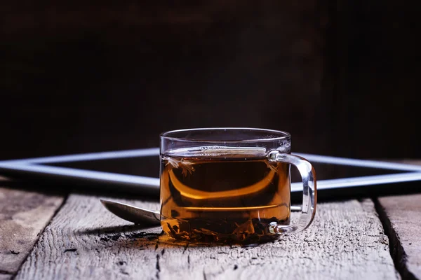 Чашка чорного гарячого чаю з ложкою та цифровим планшетом — стокове фото
