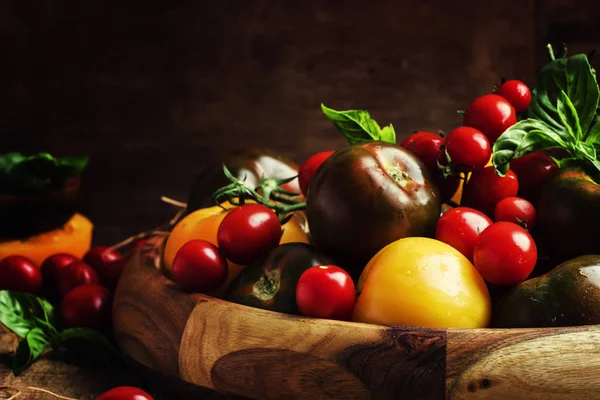 Различные помидоры на старом деревянном столе — стоковое фото