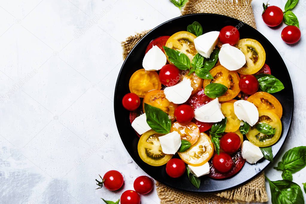 Spring salad with tomatoes, cheese and basil, gray background, top view