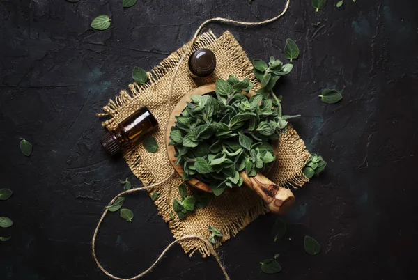 Essential oregano oil in a glass bottles and a bunch of fresh herbs, black background, top view