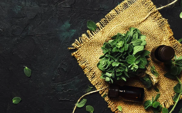 Essential oregano oil in a glass bottles and a bunch of fresh herbs, black background, top view