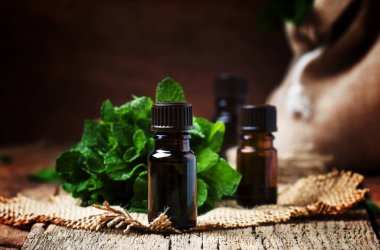 Essential oil of peppermint in a small brown bottle with fresh green mint, rustic style, vintage wooden background, selective focus clipart
