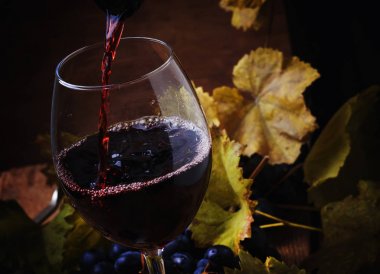 Red wine pouring into a glass, vintage wood background, selective focus clipart