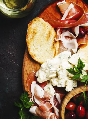Aperatifler veya antipasti, crostini, prosciutto, mavi peynir ve zeytin, siyah arka plan, görünümü top