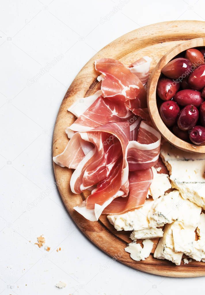 Board with appetizers, crostini, prosciutto, blue cheese and olives, gray background, top view 
