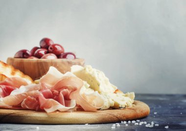 Aperatifler veya antipasti, crostini, prosciutto, mavi peynir ve zeytin, gri arka plan, seçici odak