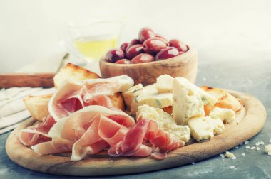 Aperatifler veya antipasti, crostini, prosciutto, mavi peynir ve zeytin, gri arka plan, seçici odak