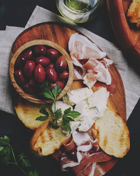 Aperatifler veya antipasti, crostini, prosciutto, mavi peynir ve zeytin, siyah arka plan, görünümü top