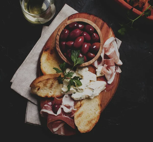 Aperatifler veya antipasti, crostini, prosciutto, mavi peynir ve zeytin, siyah arka plan, görünümü top