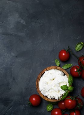 Yumuşak ricotta peyniri yeşil fesleğen ve kiraz domates, gri taş arka, üst görünümden bir ahşap kase