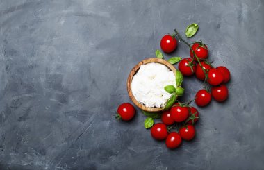 Yumuşak ricotta peyniri yeşil fesleğen ve kiraz domates, gri taş arka, üst görünümden bir ahşap kase