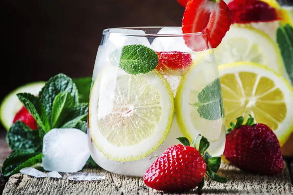 Summer iced lemonade with strawberries, lemon, mint and soda, vintage wood background, selective focus