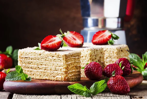 Homemade honey cake decorated with strawberries and mint, vintage wood background, selective focus