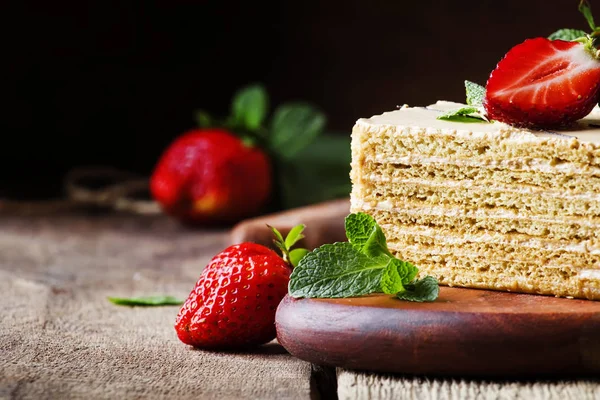 Homemade honey cake decorated with strawberries and mint, vintage wood background, selective focus