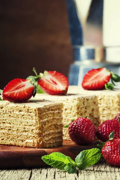 Homemade honey cake decorated with strawberries and mint, vintage wood background, selective focus
