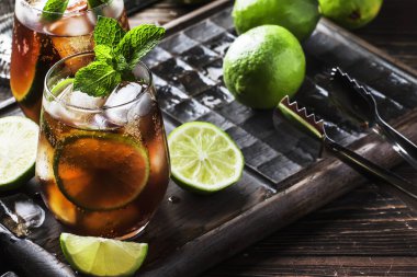 Altın rom ile Küba libre alkol kokteyl, limon suyu, kola, kireç ve buz, koyu bar sayacı arka plan, bar araçları, metin için yer