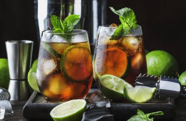 Altın rom ile Küba libre alkol kokteyl, limon suyu, kola, kireç ve buz, koyu bar sayacı arka plan, bar araçları, metin için yer