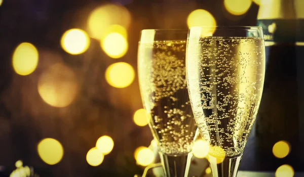 İki şampanya bardağı ve ahşap kar, altın bokeh arka planda noel süsü. Mutlu yeni yıl kutlamaları. Seçici odak ve küçük alan derinliği