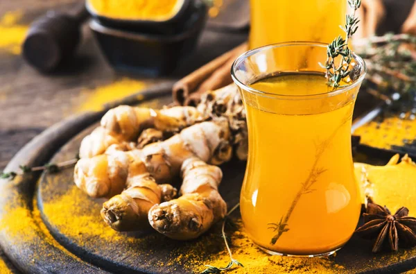 Healthy vegan turmeric golden tea with honey in glass cup on wooden tray. Herbal healing spicy tea