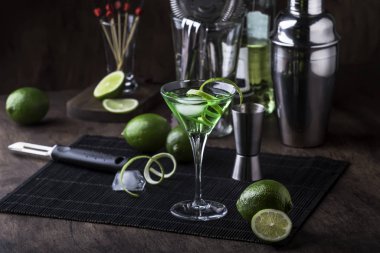 Kuru cin, vermut, limon ve buzlu yeşil alkollü kokteyl bardağı, bar aletleri, koyu arka plan.
